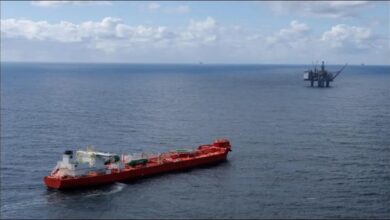 An offshore gas drilling rig stands in calm seas with a support vessel nearby.
