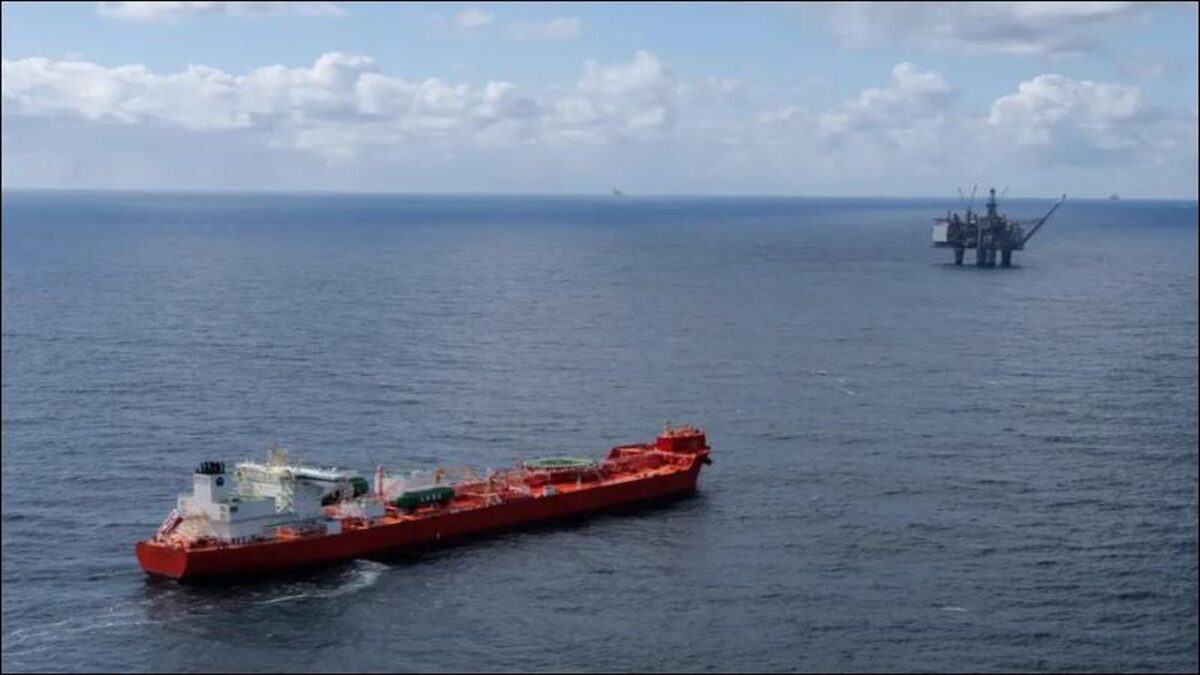 An offshore gas drilling rig stands in calm seas with a support vessel nearby.