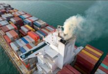 Large cargo ship emitting a thick plume of dark exhaust smoke.