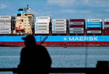A large container ship navigates a waterway, likely the Panama Canal, under a bridge.