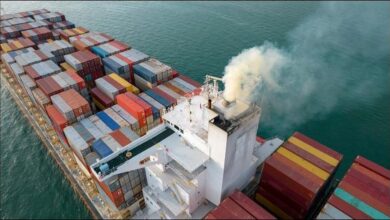 Large cargo ship emitting a thick plume of dark exhaust smoke.