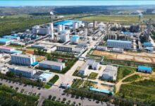 Modern green methanol plant facility with large storage tanks and ships at a port.