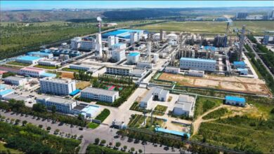 Modern green methanol plant facility with large storage tanks and ships at a port.