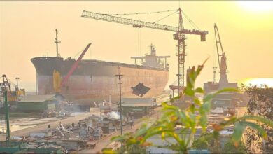 Industrial workers begin dismantling a large cargo ship at a busy recycling yard.