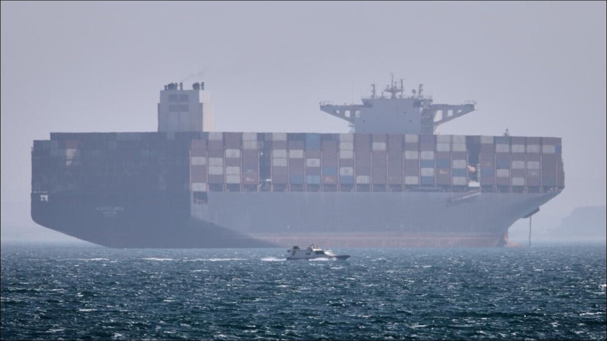 A large container ship sails, representing global shipping and geopolitical tensions in trade routes.