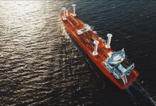 A large cargo ship with modern wind propulsion sails crosses a calm sea.