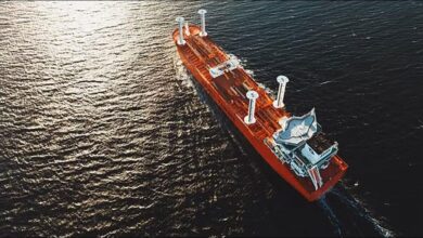 A large cargo ship with modern wind propulsion sails crosses a calm sea.