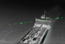 A commercial cargo ship at sea, emitting smoke and fire after an attack.