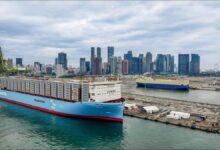 A large Maersk container ship full of containers sails past the Singapore skyline.