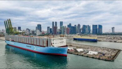 A large Maersk container ship full of containers sails past the Singapore skyline.