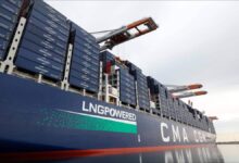 A large CMA CGM container ship is docked at a port terminal, loaded with containers.