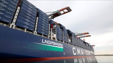 A large CMA CGM container ship is docked at a port terminal, loaded with containers.