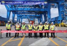 Officials cut a ribbon at Port Everglades, commissioning new container cranes with a large cargo ship nearby.