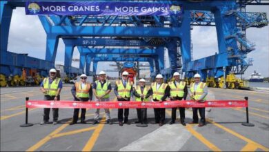 Officials cut a ribbon at Port Everglades, commissioning new container cranes with a large cargo ship nearby.