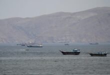 A large oil tanker navigates a strait with land visible on the horizon.
