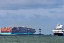 A large container ship with stacked cargo containers sails across the ocean.