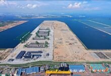 Container cranes load a large cargo ship at a busy, modern port filled with stacked containers.