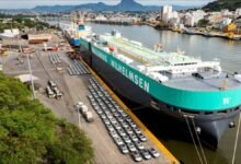 A large car carrier vessel docked at port, surrounded by numerous cars.