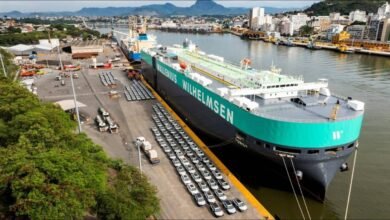 A large car carrier vessel docked at port, surrounded by numerous cars.