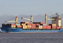 The feeder containership M/V Joanna sails on calm blue waters under a bright sky.