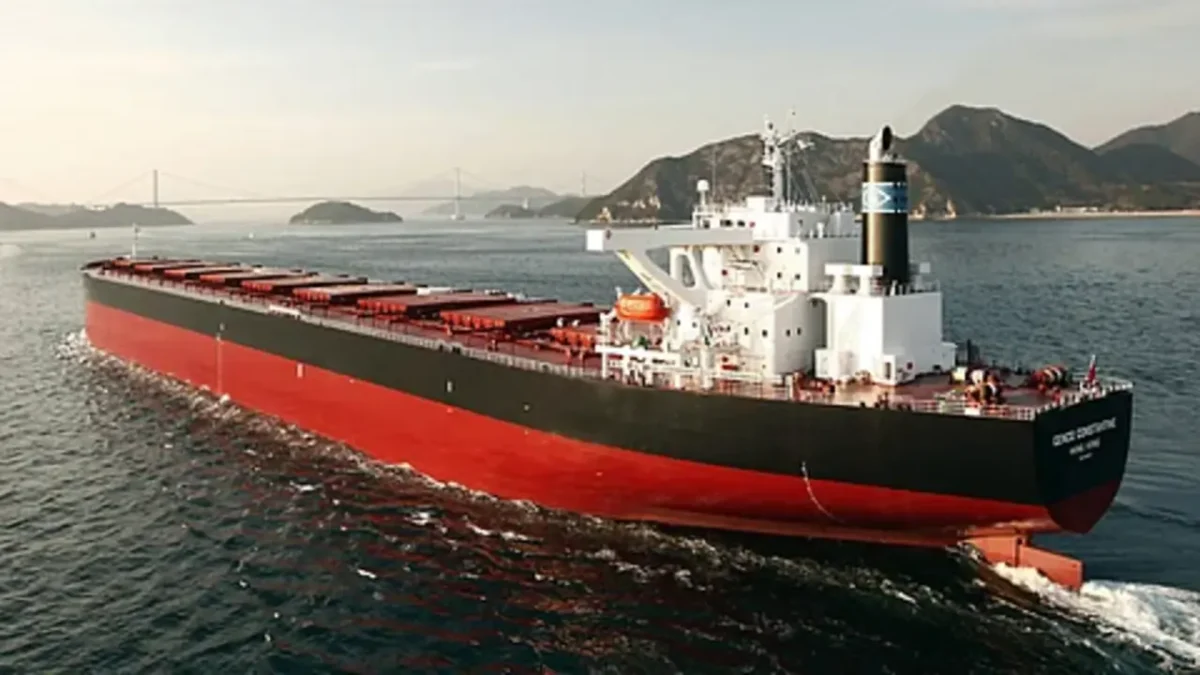 A large Newcastlemax bulk carrier ship sails on the open ocean.