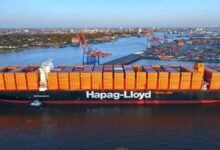 A large Hapag-Lloyd container ship docked at a port terminal.