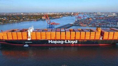 A large Hapag-Lloyd container ship docked at a port terminal.