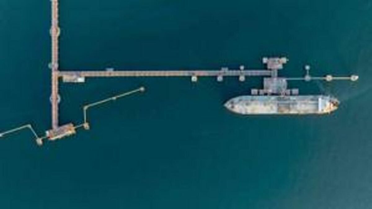 A large container ship docked at a modern deep-water port with cranes and stacked containers.
