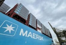 A large Maersk container ship navigates the sea, packed with shipping containers.