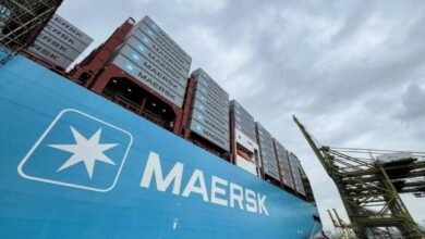 A large Maersk container ship sails at sea, loaded with containers.