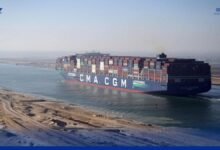 A massive container ship transits the Suez Canal under a clear sky.